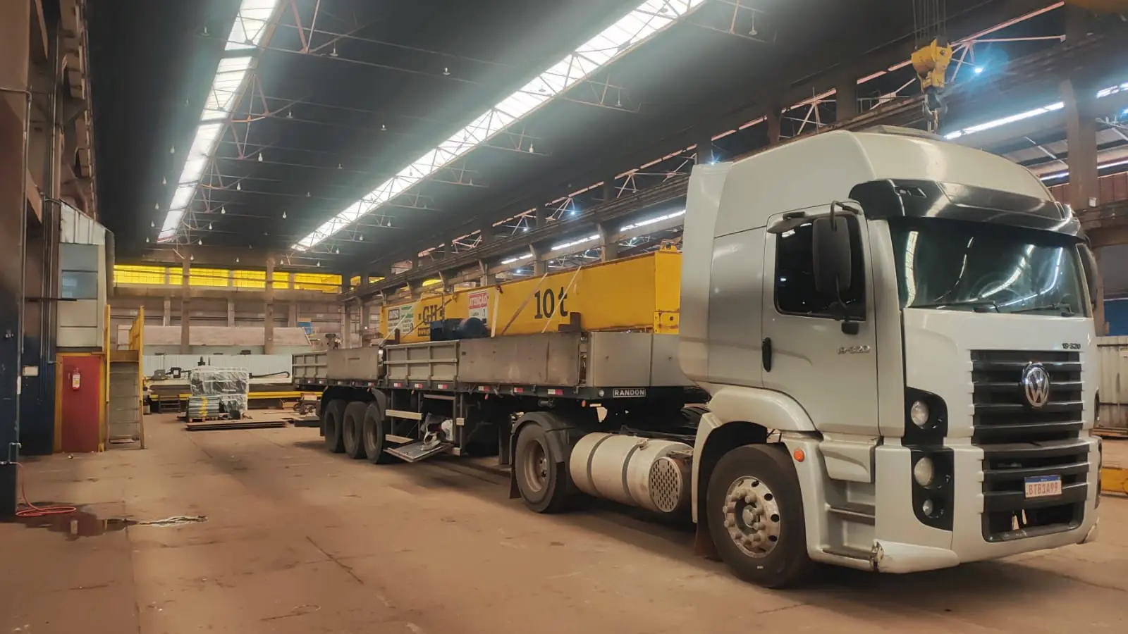 Caminhão recebendo equipamento industrial durante carregamento dentro de fábrica