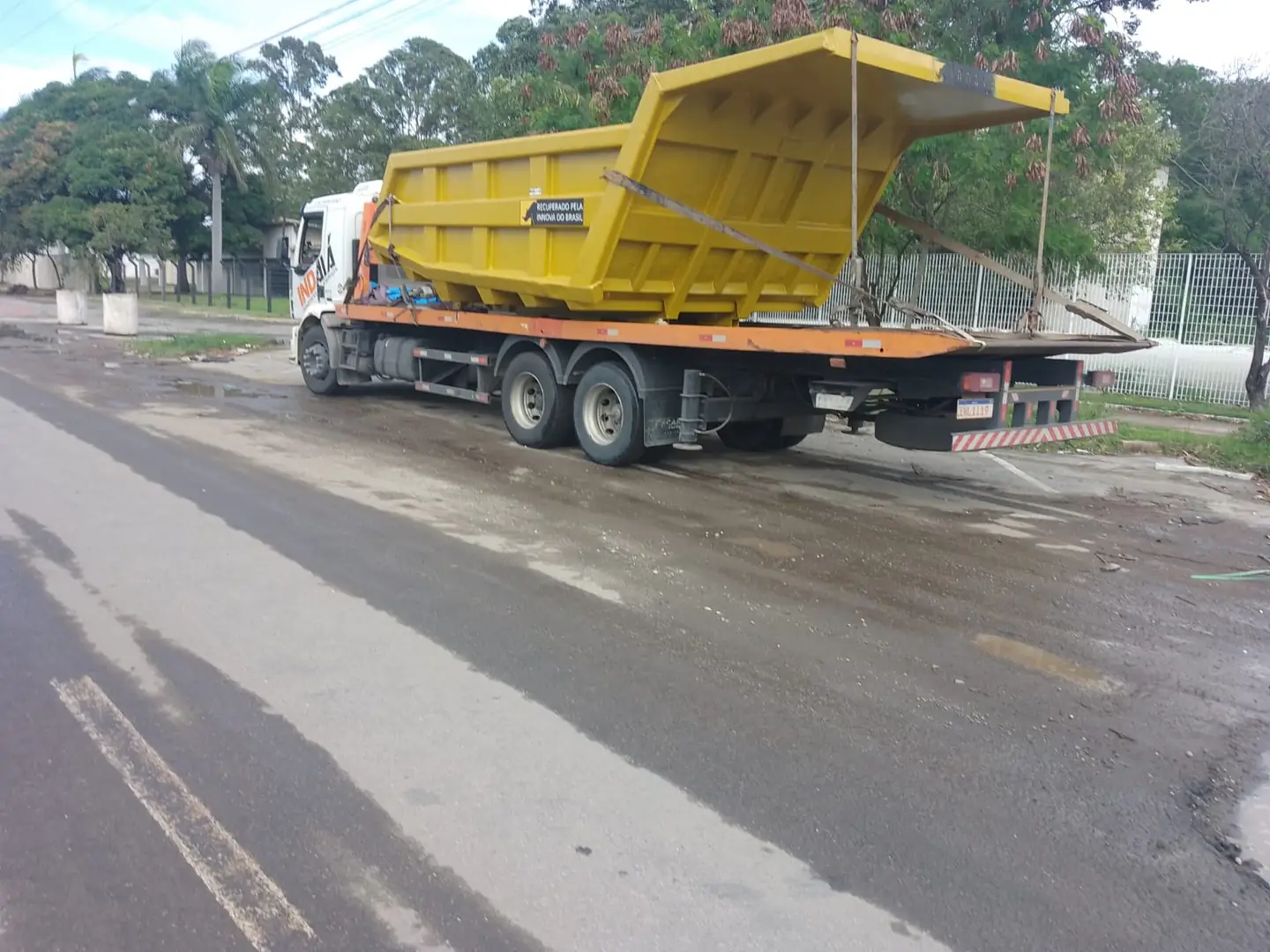 Implemento amarelo de grande porte transportado em caminhão plataforma